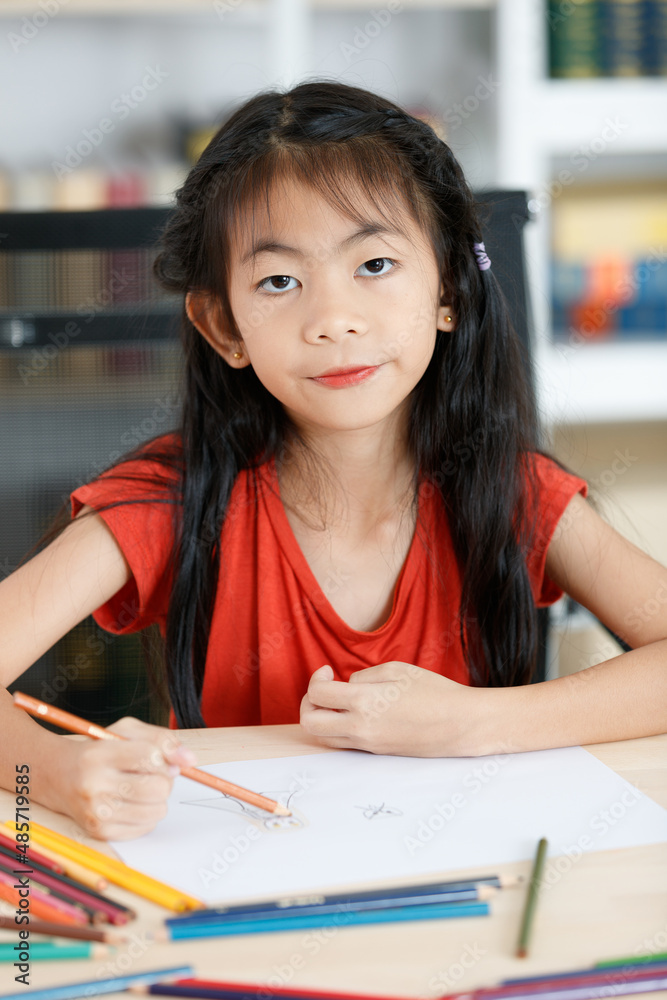 Asian creative young primary school girl artist in casual outfit sitting using color pencil drawing painting picture at home school classroom lesson in living room during pandemic quarantine period
