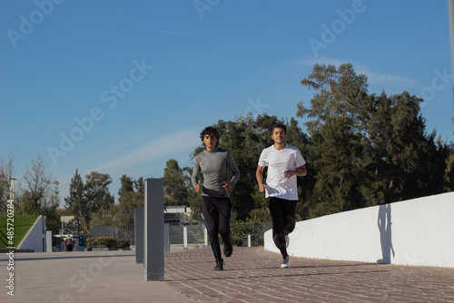 two young latin male runners training together in the park in the morning sunshine
