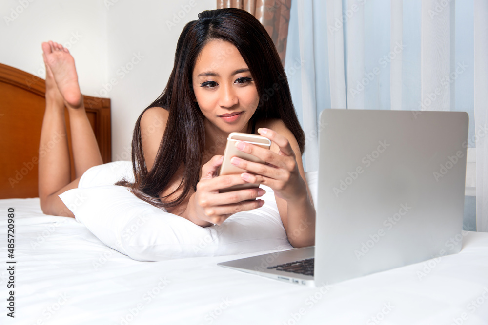 Asian woman lying down while using mobile phone and laptop Asian woman lying down while using mobile phone and laptop