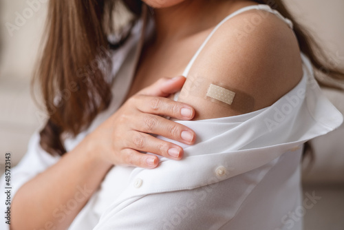 Closeup image of a young woman with adhesive bandage, medical plaster, band aid on her shoulder for vaccination concept photo