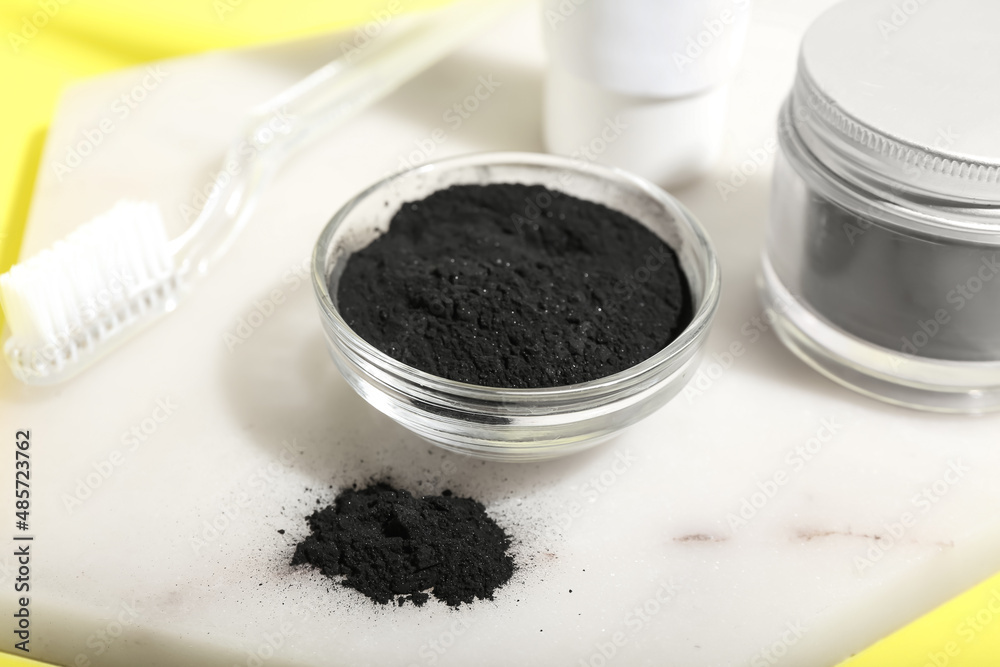 Bowl with activated charcoal tooth powder and toothbrush on yellow background, closeup Bowl with activated charcoal tooth powder and toothbrush on yellow background, closeup