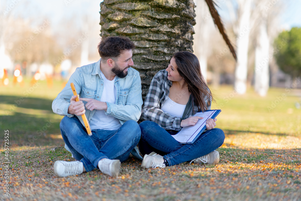 two happy students celebrating final exams result pointing fingers sitting in park two happy students celebrating final exams result pointing fingers sitting in park