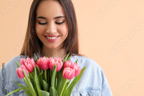 Happy young woman with bouquet of tulips on beige background. International Women's Day