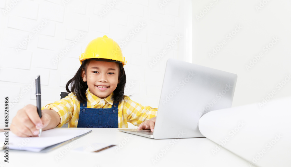 Asian young little girl dreaming about future job career as engineering wearing yellow safety hardhat helmet sitting on working table with laptop computer blueprint smartphone and paper clipboard Asian young little girl dreaming about future job career as engineering wearing yellow safety hardhat helmet sitting on working table with laptop computer blueprint smartphone and paper clipboard