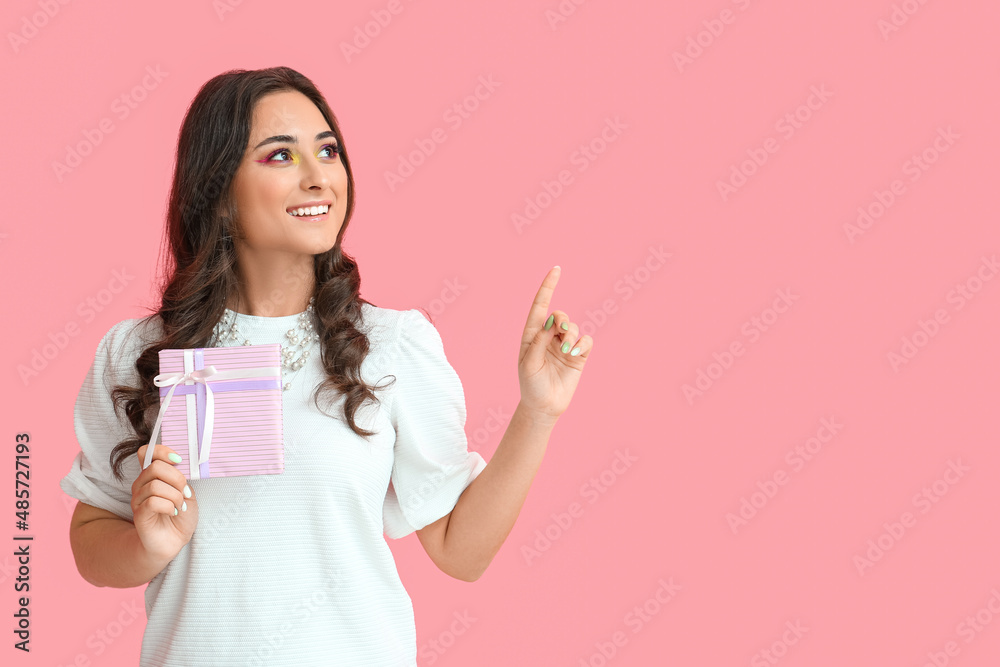 Woman with creative makeup holding gift box and pointing at something on pink background. International Women's Day Woman with creative makeup holding gift box and pointing at something on pink background. International Women's Day