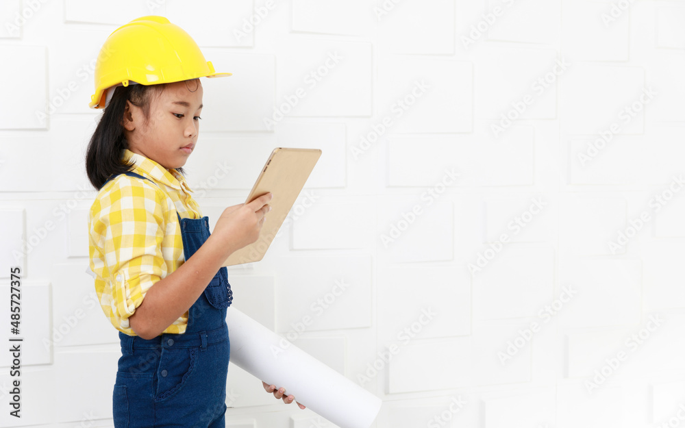 Portrait studio shot Asian young little elementary schoolgirl future dream job career as engineer and architect wears yellow safety hardhat helmet standing look at camera holding tablet and blueprint Portrait studio shot Asian young little elementary schoolgirl future dream job career as engineer and architect wears yellow safety hardhat helmet standing look at camera holding tablet and blueprint