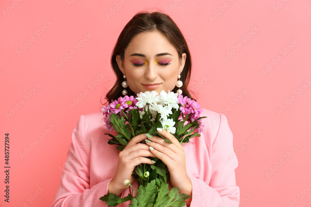 Woman with creative makeup holding bouquet of flowers on pink background. International Women's Day