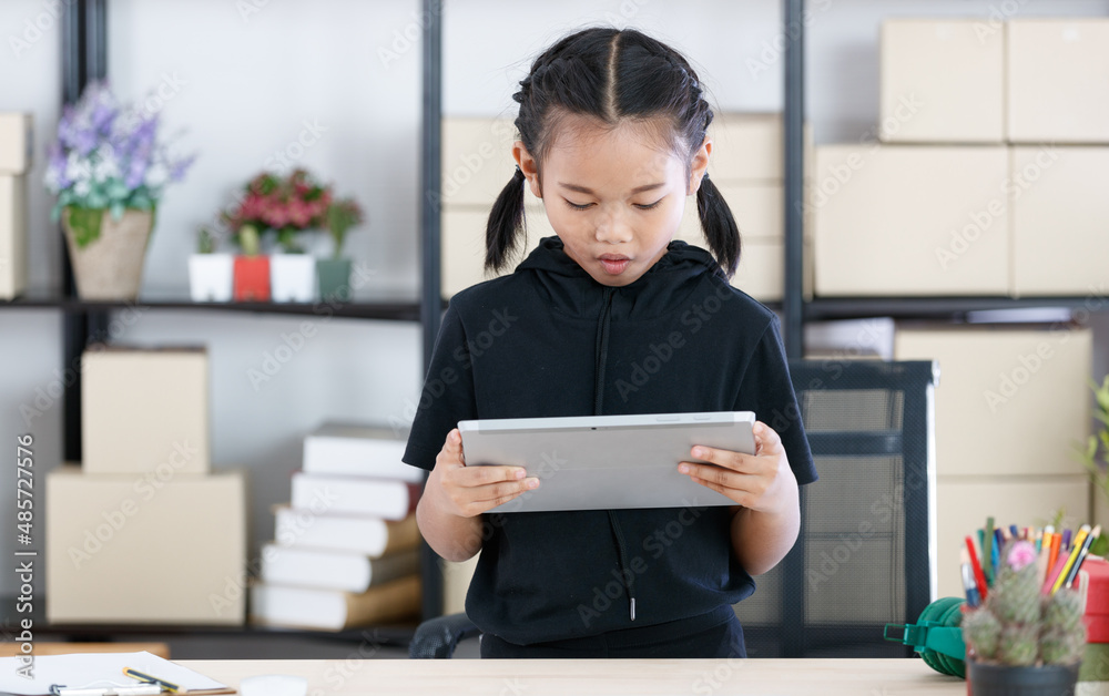 Portrait shot of Asian young primary schoolgirl in casual outfit standing smiling holding showing tablet computer in hands for advertising copy space and text Portrait shot of Asian young primary schoolgirl in casual outfit standing smiling holding showing tablet computer in hands for advertising copy space and text