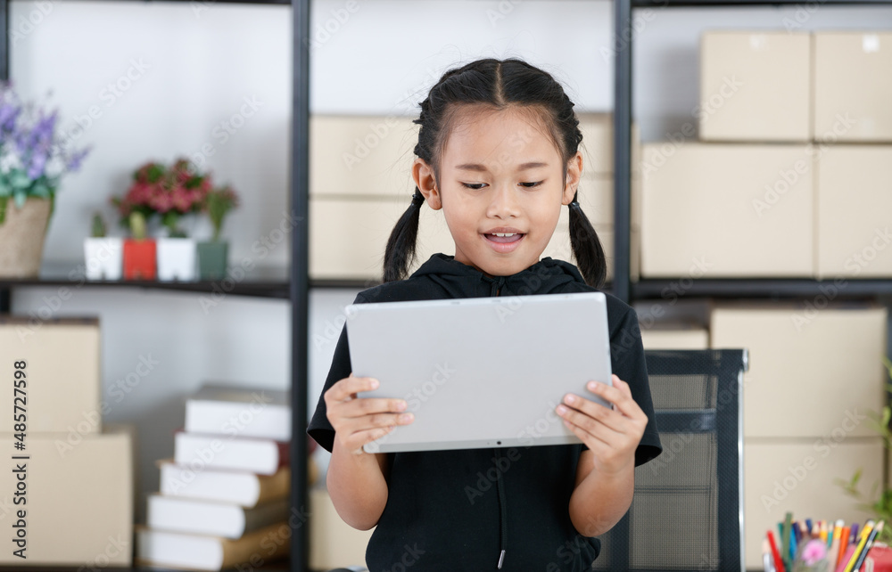 Portrait shot of Asian young primary schoolgirl in casual outfit standing smiling holding showing tablet computer in hands for advertising copy space and text Portrait shot of Asian young primary schoolgirl in casual outfit standing smiling holding showing tablet computer in hands for advertising copy space and text