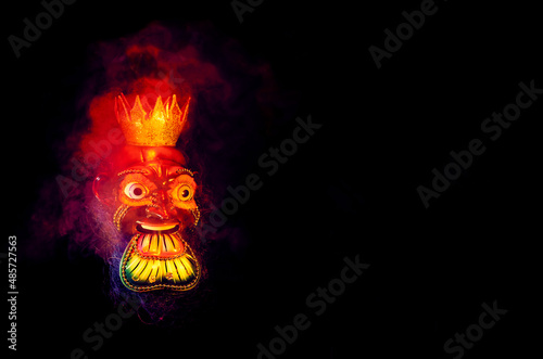 Beautiful mask of a traditional feast, surrounded by colorful smoke, with black background and copy.