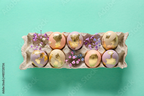Holder with beautiful Easter eggs and gypsophila flowers on color background