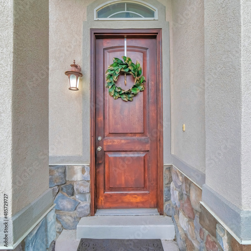 Square Wooden front door of a house with transom window and leafy wreath at the front