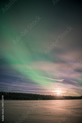 Northern Lights (aurora borealis) and moon, seen over a snow covered lake in winter in Finnish Lapland, inside Arctic Circle in Finland