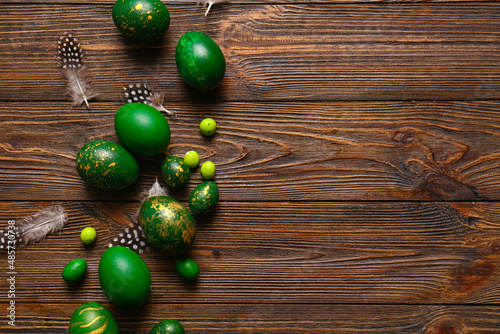 Stylish Easter eggs and feathers on wooden background