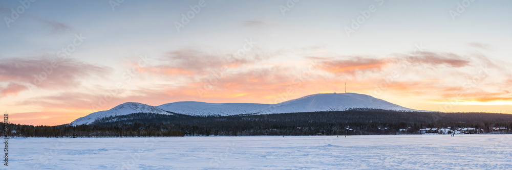 Cold weather and snow covered icy winter landscape with dramatic sunset sky and clouds over a frozen lake inside the Arctic Circle in Lapland in Finland