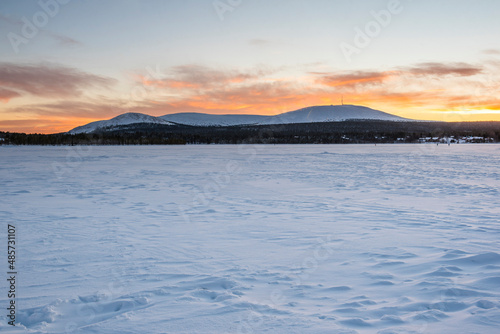 Cold weather and snow covered icy winter landscape with dramatic sunset sky and clouds over a frozen lake inside the Arctic Circle in Lapland in Finland