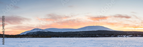 Cold weather and snow covered icy winter landscape with dramatic sunset sky and clouds over a frozen lake inside the Arctic Circle in Lapland in Finland