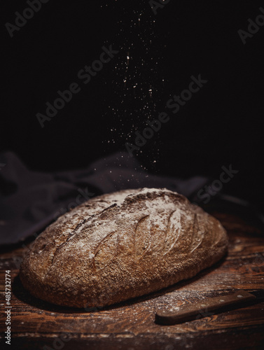 bread on a dining wooden table. homemade bread from the oven. round wholegrain bread on a dark background sprinkled with flour
