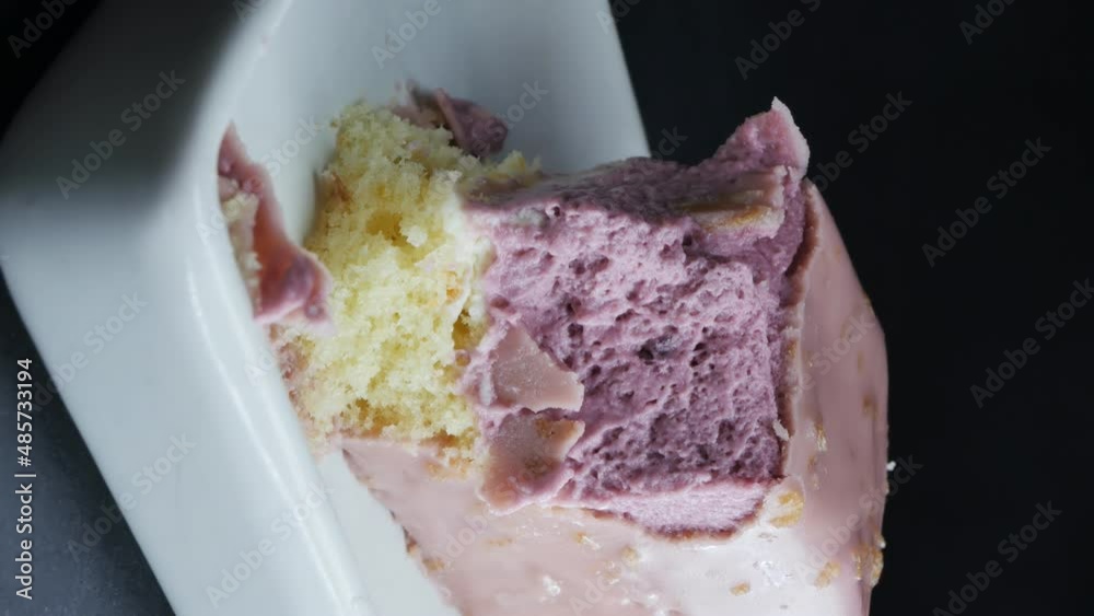 vertical screen. a white porcelain spoon breaks off a purple glazed mousse cake in a white ceramic rectangular bowl vertical screen. a white porcelain spoon breaks off a purple glazed mousse cake in a white ceramic rectangular bowl