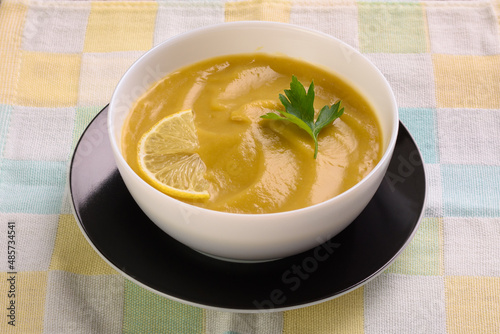 Vegetable soup puree with parsley and lemon in a white cup is on a colored napkin