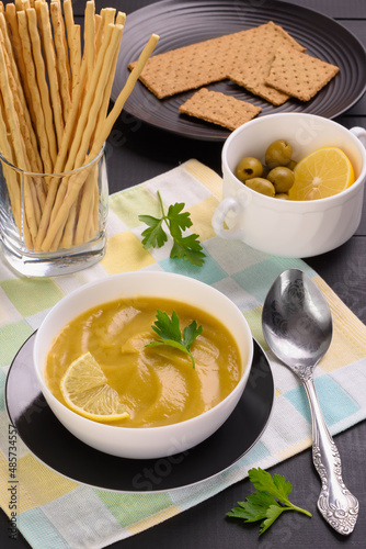 Vegetable soup with parsley and lemon in a white bowl on the table. Vertical frame.