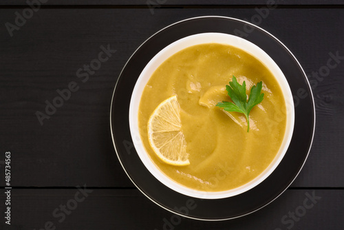 Vegetable soup with parsley and lemon in a white bowl on the table.