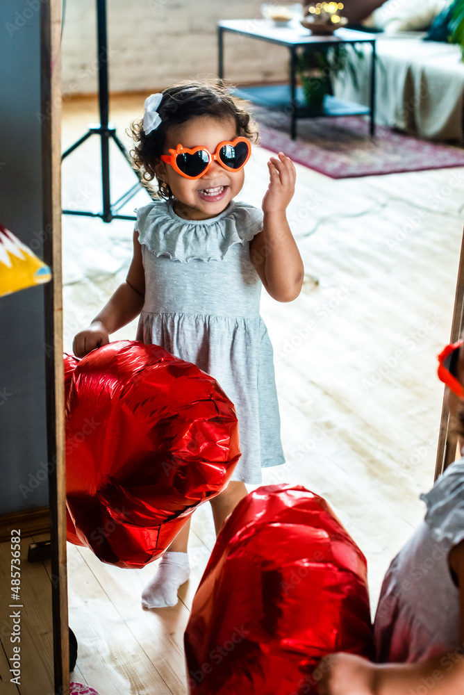 Obraz premium girl with dark, black skin color, celebrate valentine's day. heart shaped red foil balloons and glasses