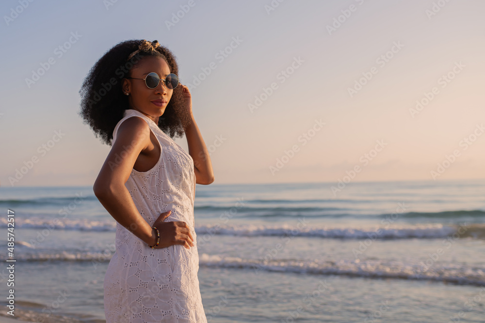 Woman wearing sunglasses on the beach in summer clothes looking back at the camera Woman wearing sunglasses on the beach in summer clothes looking back at the camera