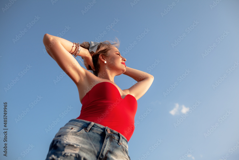 The portrait of woman wearing summer clothes posing against blue sky The portrait of woman wearing summer clothes posing against blue sky