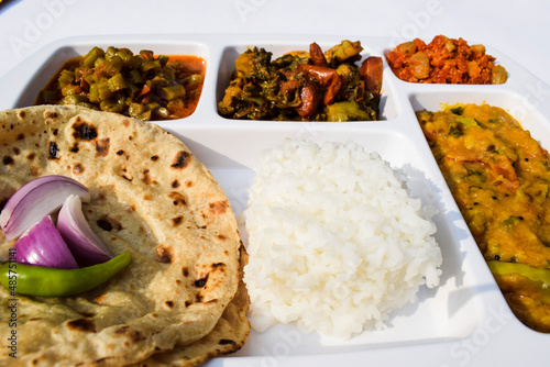 Indian Simple homemade lunch of Roti, sabji with mix veg brinjal potato curry and french beans curry, dal and gaajar halwa. complete simple home cooked meal thaali on white background photo