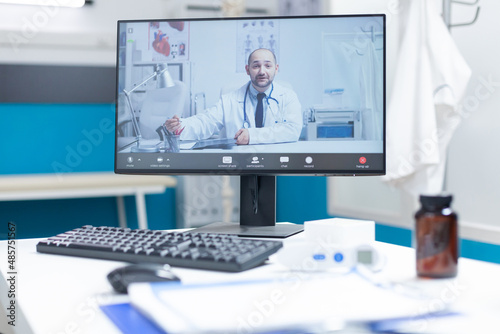 Computer with medical videocall conference meeting on screen standing on table in empty doctor office with nobody in it. Remote doctor during clinical examination. Health care support call