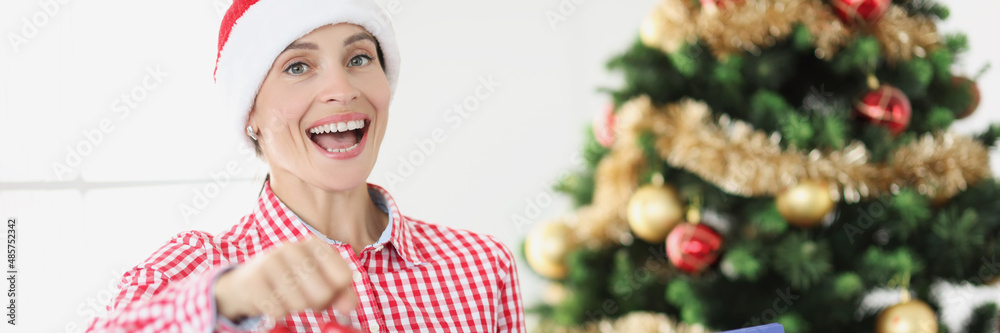 Portrait of young smiling woman in santa claus hat hold alarm clock and business documents on background