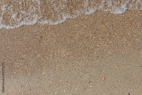 Close-up of sea foam on the sand beach with summer sunlight