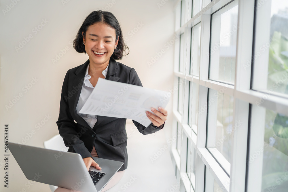business woman smiling with holding paper and using laptop in office business woman smiling with holding paper and using laptop in office