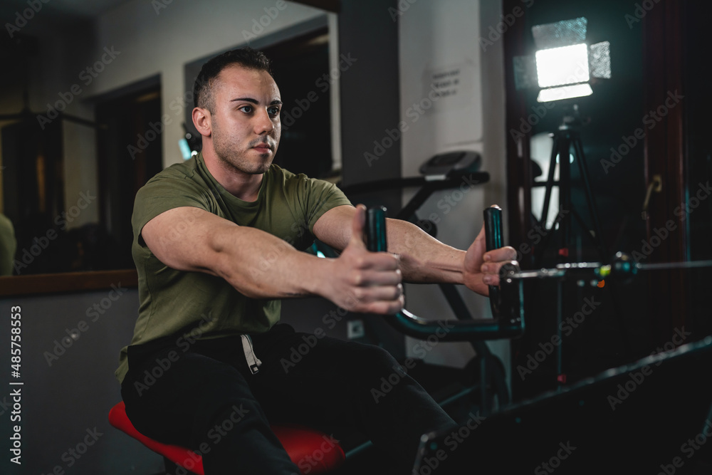 One man young adult caucasian male bodybuilder training back on the cable crossover exercise machine in the gym wearing shirt dark photo real people copy space One man young adult caucasian male bodybuilder training back on the cable crossover exercise machine in the gym wearing shirt dark photo real people copy space