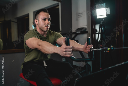 One man young adult caucasian male bodybuilder training back on the cable crossover exercise machine in the gym wearing shirt dark photo real people copy space
