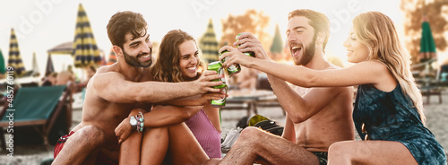 Joyful young friends toasting with canned beers on the beach