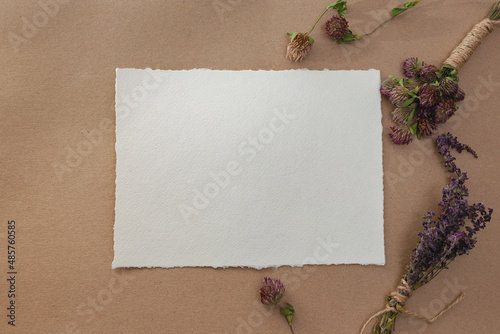 Blank paper mockup of watercolor paper with dry herbs on table against craft paper background 