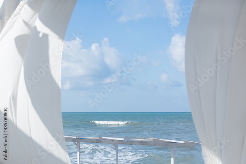 View of sea or ocean from summer terrace or veranda. White curtains shaken by the wind. Blue sky with clouds in summer. Blurred photo background, fog view
