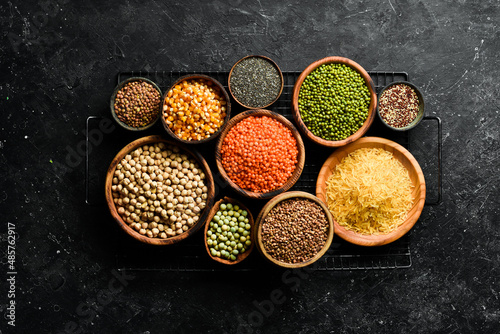 Legumes, a set consisting of different types of beans, lentils and peas, rice and buckwheat on a black background, top view. The concept of healthy and nutritious food