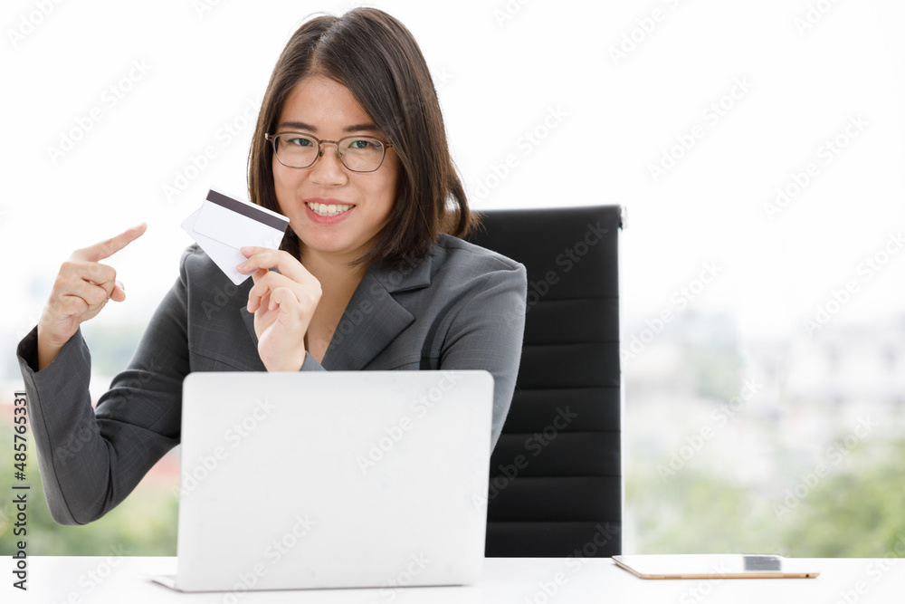 Portrait shot of Asian happy female employee staff sitting smiling holding pointing credit card in hand while shopping from online store via laptop notebook computer in company office during working Portrait shot of Asian happy female employee staff sitting smiling holding pointing credit card in hand while shopping from online store via laptop notebook computer in company office during working