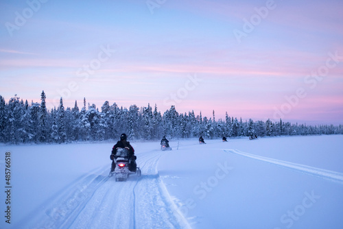 Snowmobiling on the frozen lake at sunset at Torassieppi, Lapland, Finland