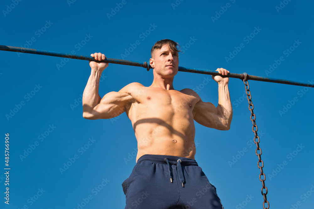 Muscular man working out in an outdoor gym, doing pull-ups.