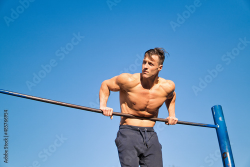 Muscular man working out in an outdoor gym, doing pull-ups.