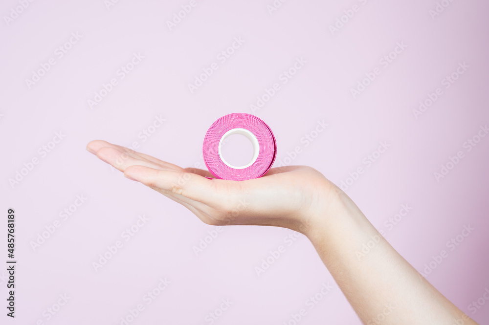 Woman hand holding kinesio tapes isolated on pink. Kinesiology, physical therapy, rehabilitation concept Woman hand holding kinesio tapes isolated on pink. Kinesiology, physical therapy, rehabilitation concept