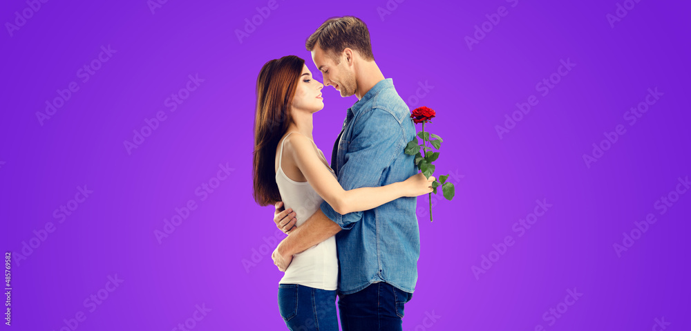 Love, relationship, dating, flirting, romantic concept - amorous hugging couple with flower, standing close to each other, purple violet background. Valentines Day holiday. Copy space.
