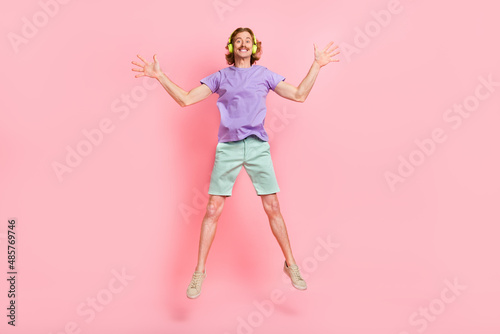 Full length body size view of attractive cheerful guy jumping listening song hit having fun isolated over pink pastel color background photo