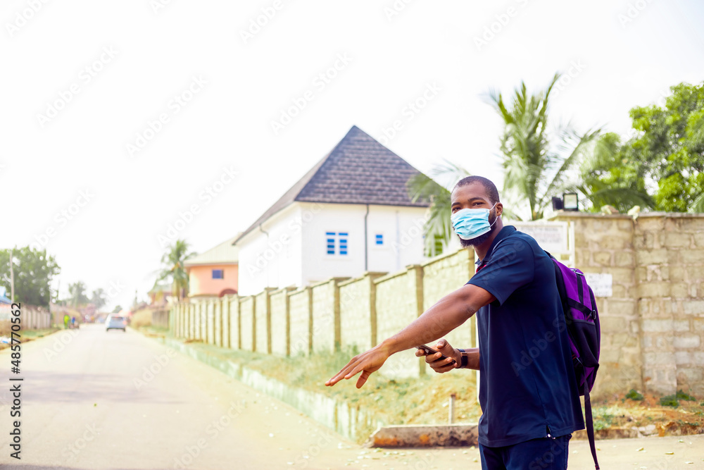black man wearing nose mask calling cab carrying school backpack holding mobilephone