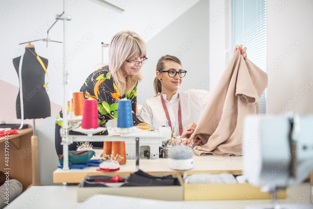 Positive working environment as two female tailors check the quality of their work in a small workshop Positive working environment as two female tailors check the quality of their work in a small workshop