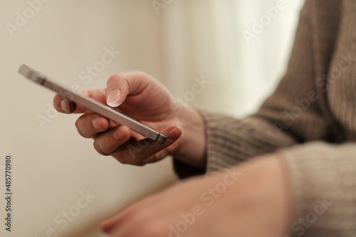 Closeup of female hands using smartphone for communication in living room